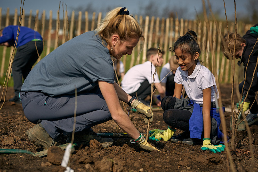 Earthwatch UK volunteer planting a sapling with a child during a community Tiny Forest project