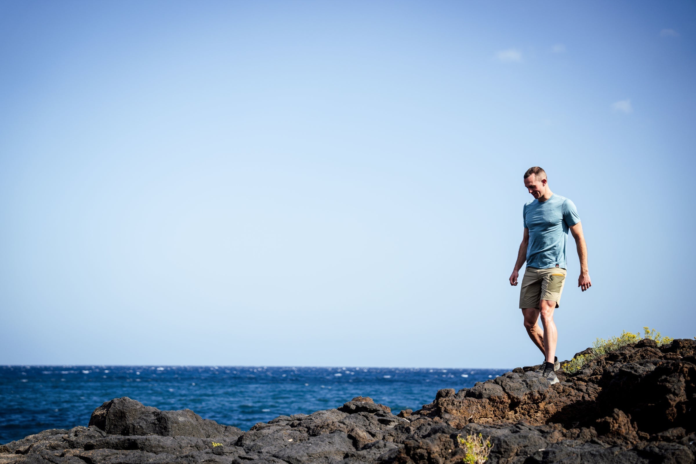 Man walking along volcanic rocks by the sea in Isobaa Merino tee