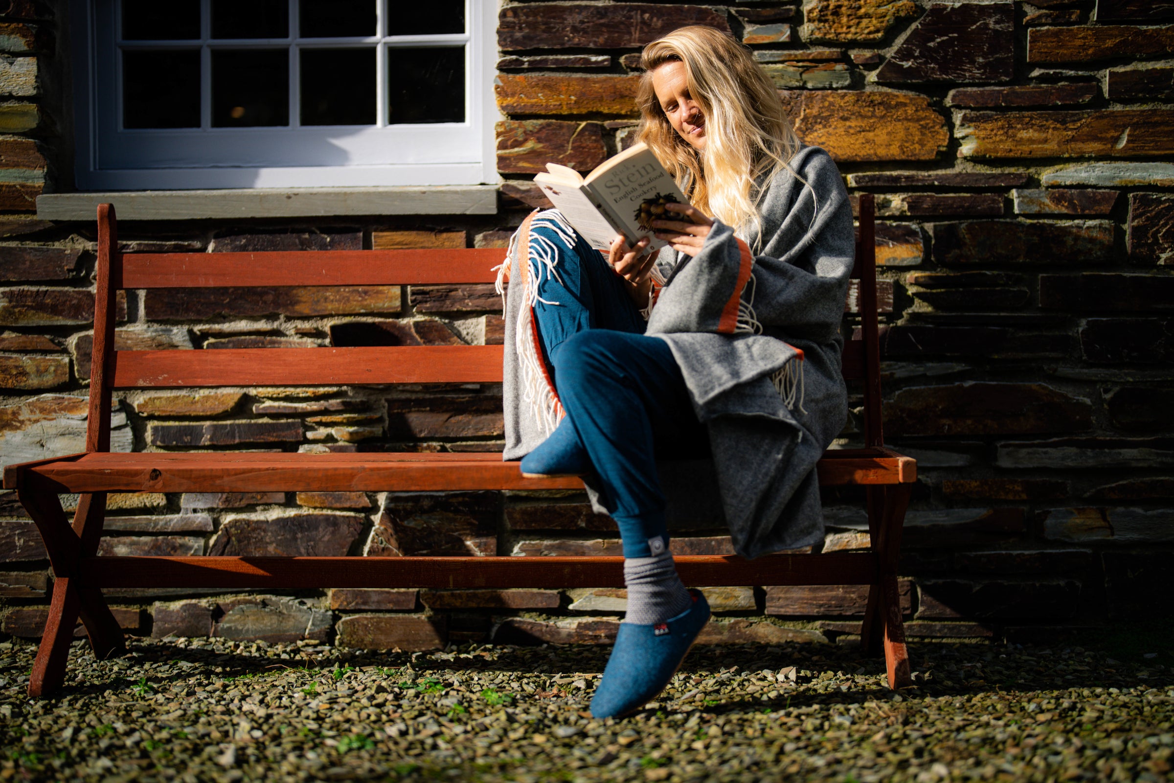 Person reading on a bench wrapped in an Isobaa Merino Throw