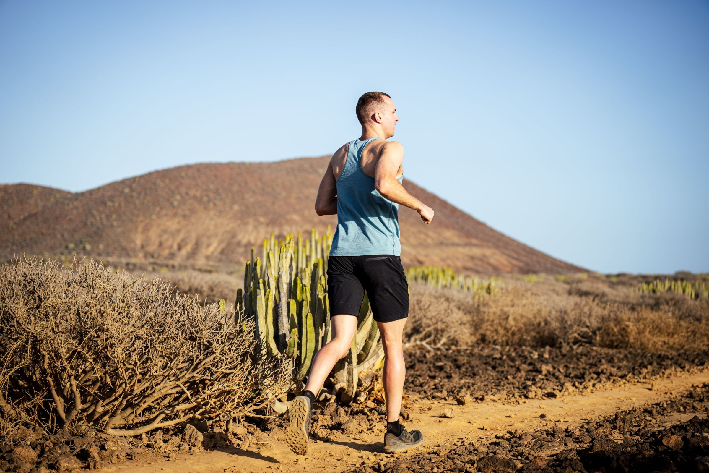 Man trail running through a dry, rocky landscape in a Merino vest top and shorts