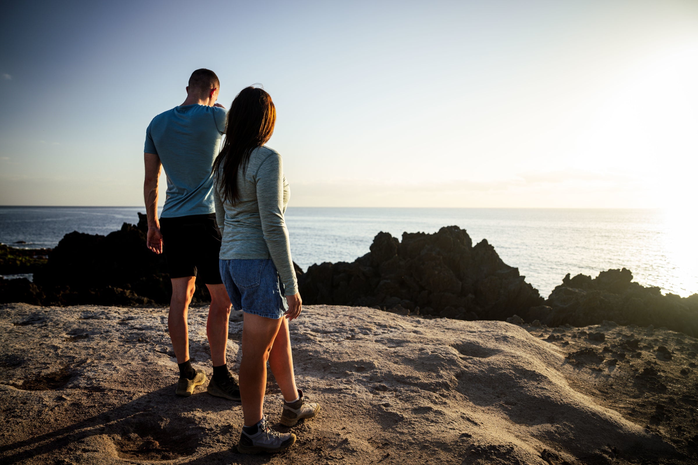 Man and woman looking out at the ocean during sunset in lightweight Merino clothing