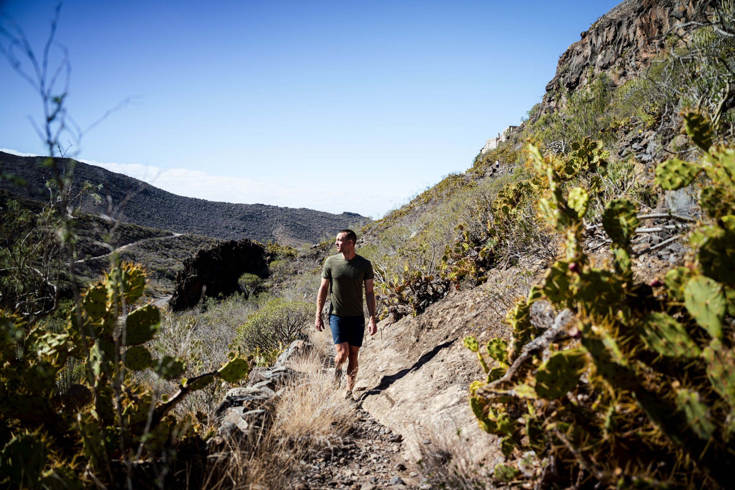 Man walking through a desert mountain trail wearing a green Merino tee
