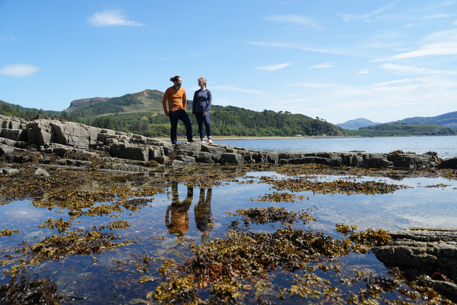 Two people standing on coastal rocks by calm water