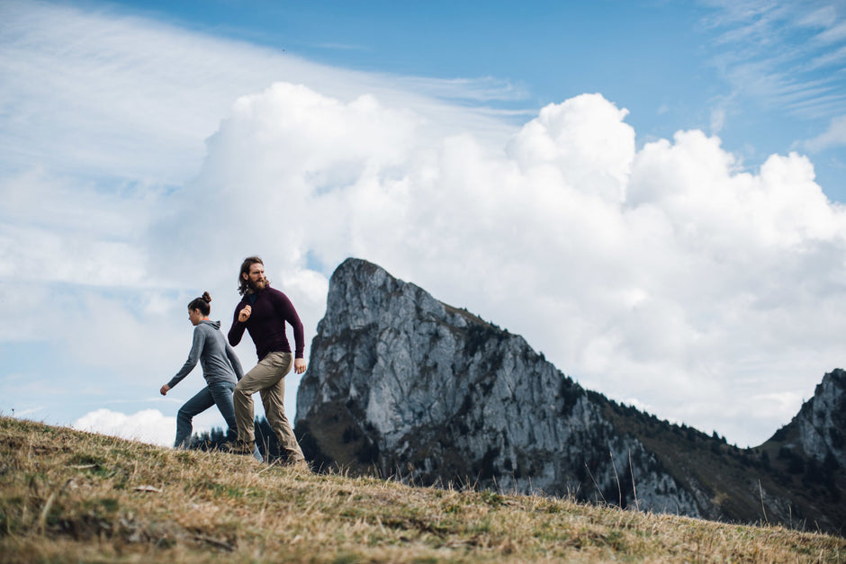 Two people hiking on a grassy hill with a mountain in the background