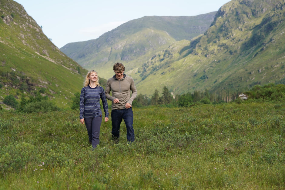Two people walking through a grassy field with mountains in the background