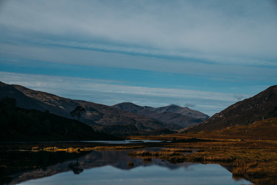 Mountain landscape with hills, water, and open moorland under a blue sky