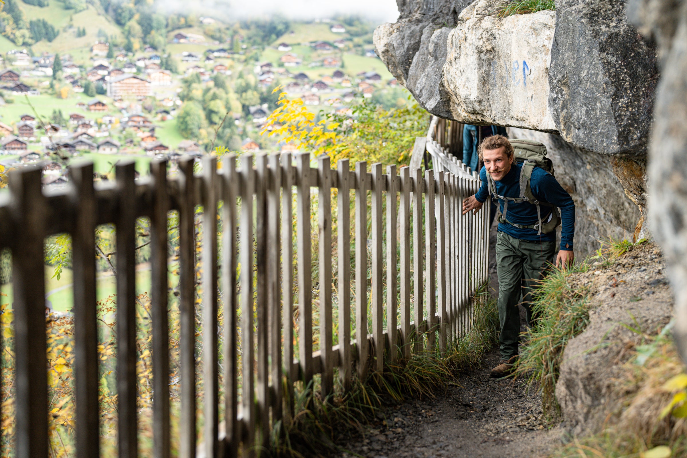 Hiker with backpack ducking under a rock overhang on a narrow mountain trail