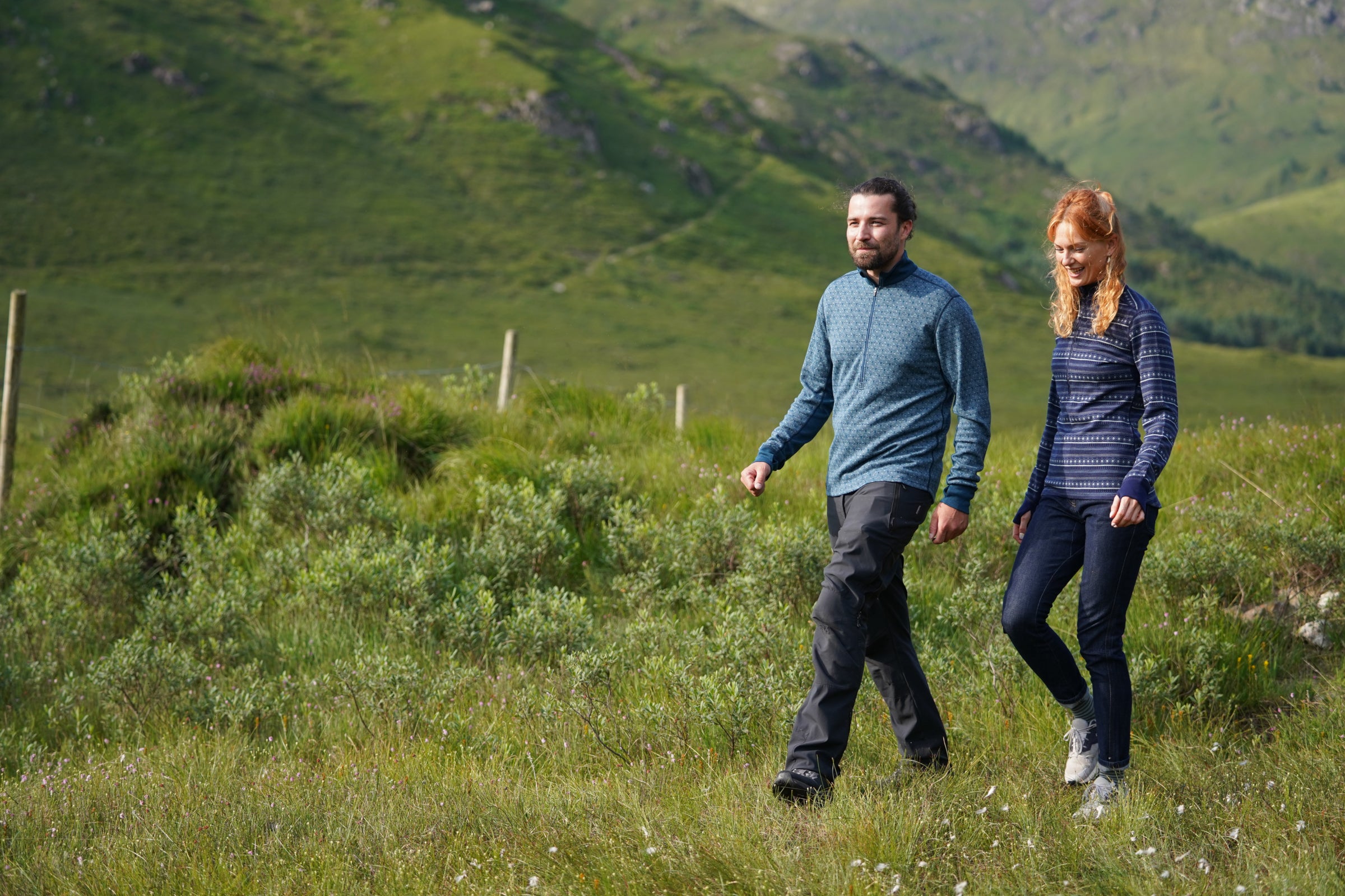 Two people walking in a grassy field with mountains in the background