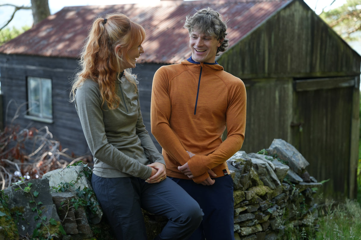 A man and a woman sitting outdoors next to a rustic stone wall and wooden shed