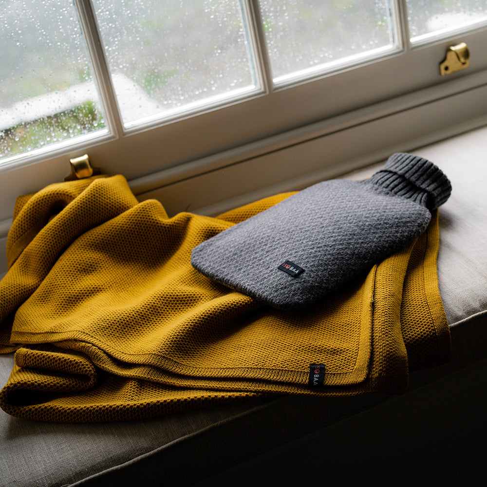 Isobaa | Merino Jacquard Hot Water Bottle Cover (Charcoal/Smoke) | Say goodbye to ordinary hot water bottles! You'll love the luxurious feel of our Merino wool cover – and your skin will thank you! Wrap yourself in cosy warmth, enjoy natural breathability, and discover the ultimate hot water bottle indulgence.