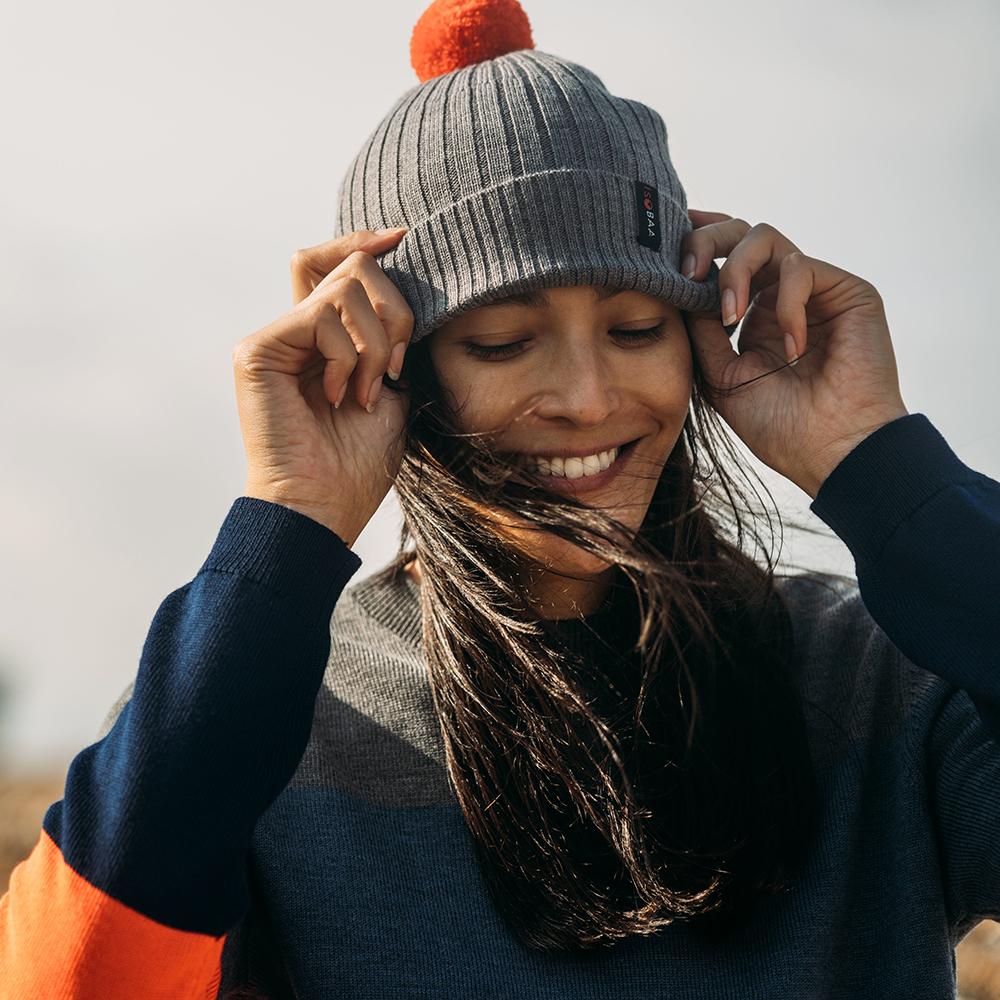 Isobaa | Merino Bobble Beanie (Charcoal/Orange) | Stay warm and stylish with Isobaa's extra-fine Merino bobble beanie! Its cosy warmth, playful bobble, and classic rib-knit design will make it your go-to winter essential for hikes, city strolls, and everything in between.