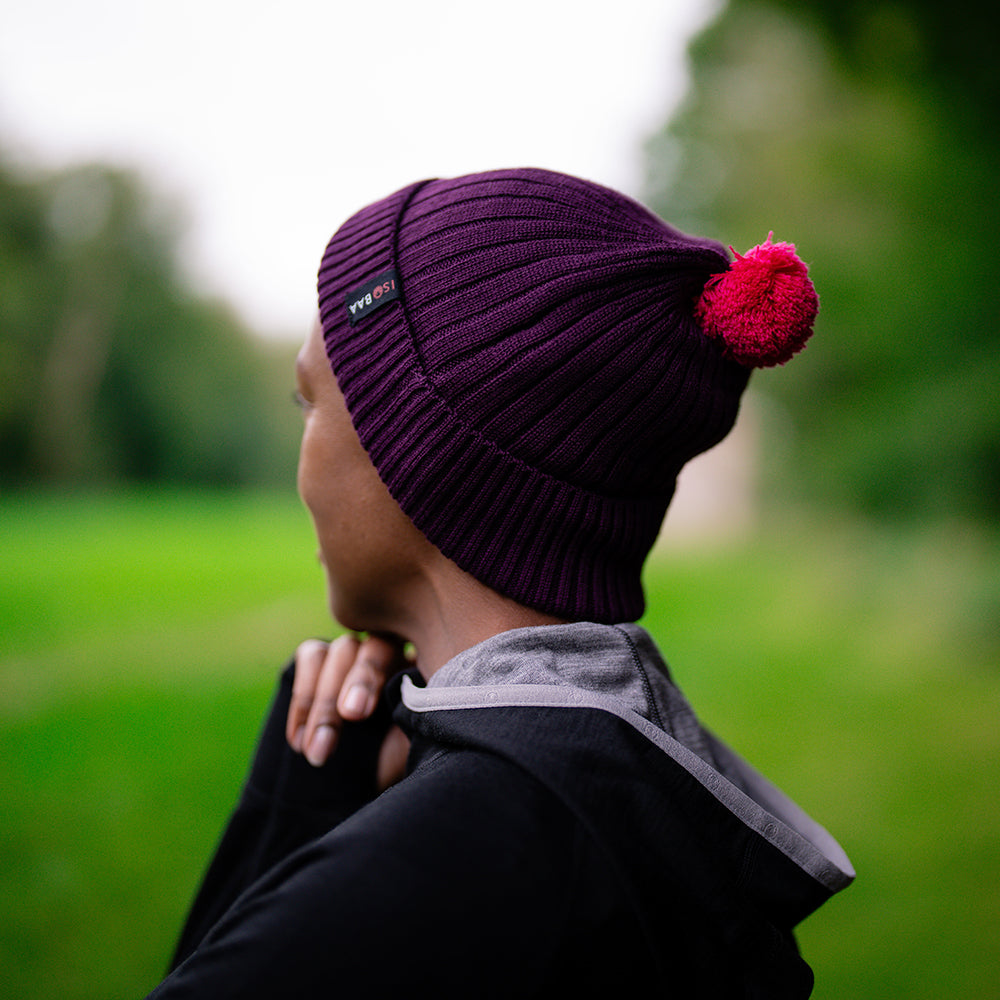 Isobaa | Merino Bobble Beanie (Wine/Fuchsia) | Stay warm and stylish with Isobaa's extra-fine Merino bobble beanie! Its cosy warmth, playful bobble, and classic rib-knit design will make it your go-to winter essential for hikes, city strolls, and everything in between.