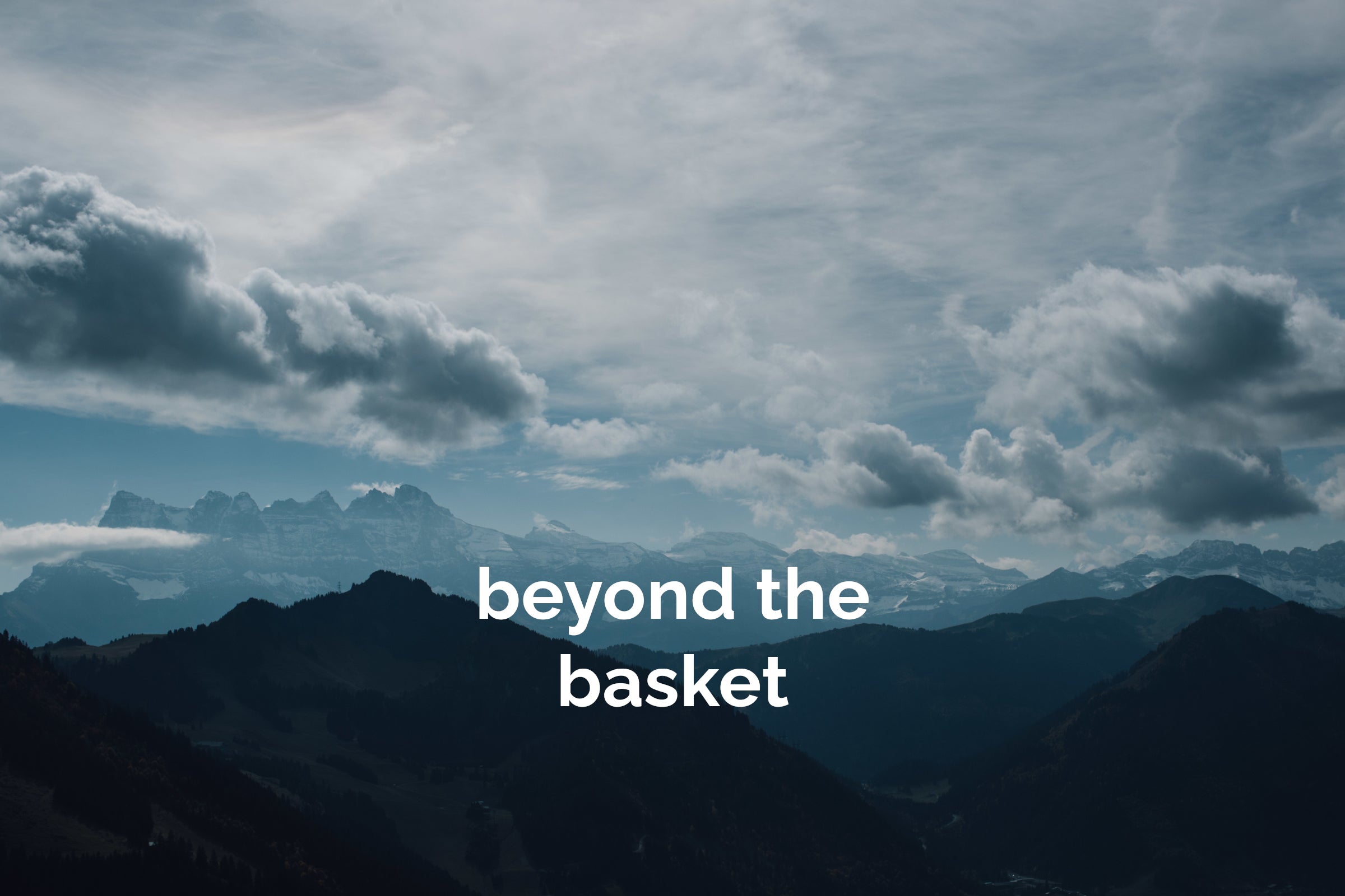 A mountain landscape under a cloudy sky with the phrase "beyond the basket" overlaid in the center in white text