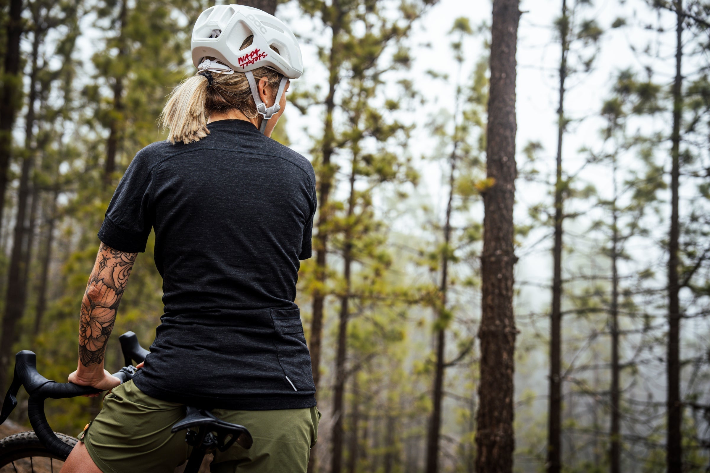 Cyclist wearing a dark merino T-shirt and helmet, paused in a misty pine forest