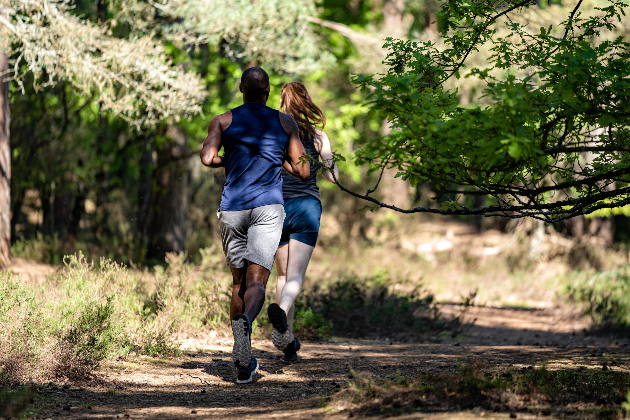 A man and a woman jogging on a forest trail, both dressed in merino activewear by Isobaa