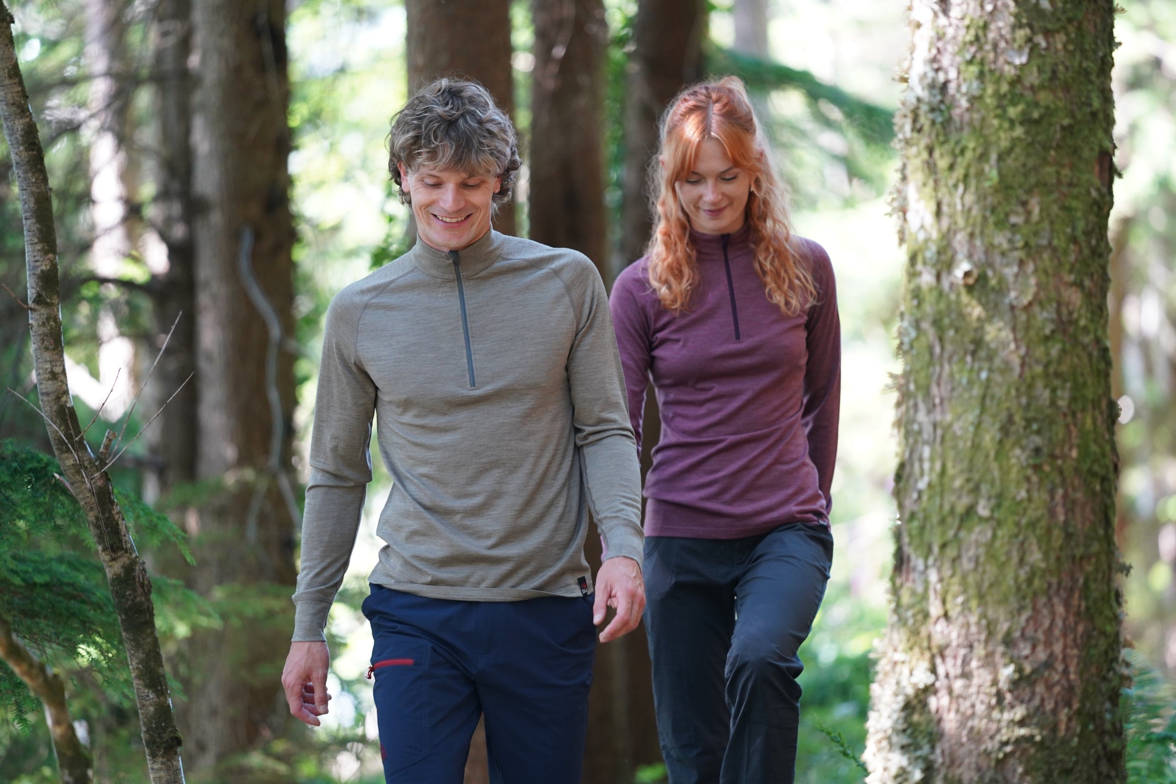 Two people walking through a forest wearing merino clothing