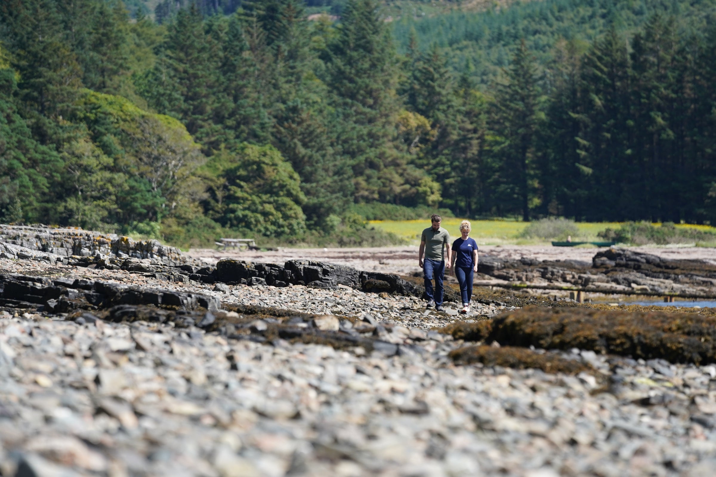 Two people walking on a rocky shoreline wearing Isobaa tops