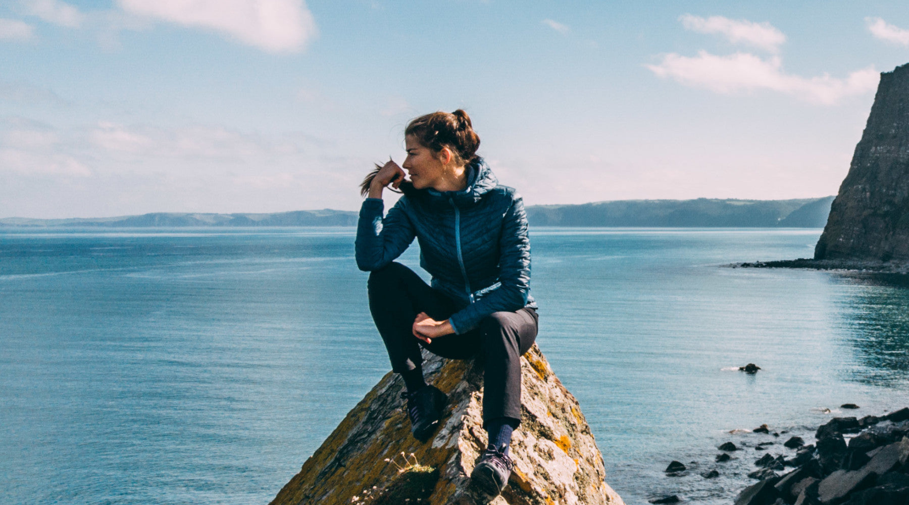 Isobaa Merino Wool Insulated Jacket sat on a rocky cliffside next to the calm ocean