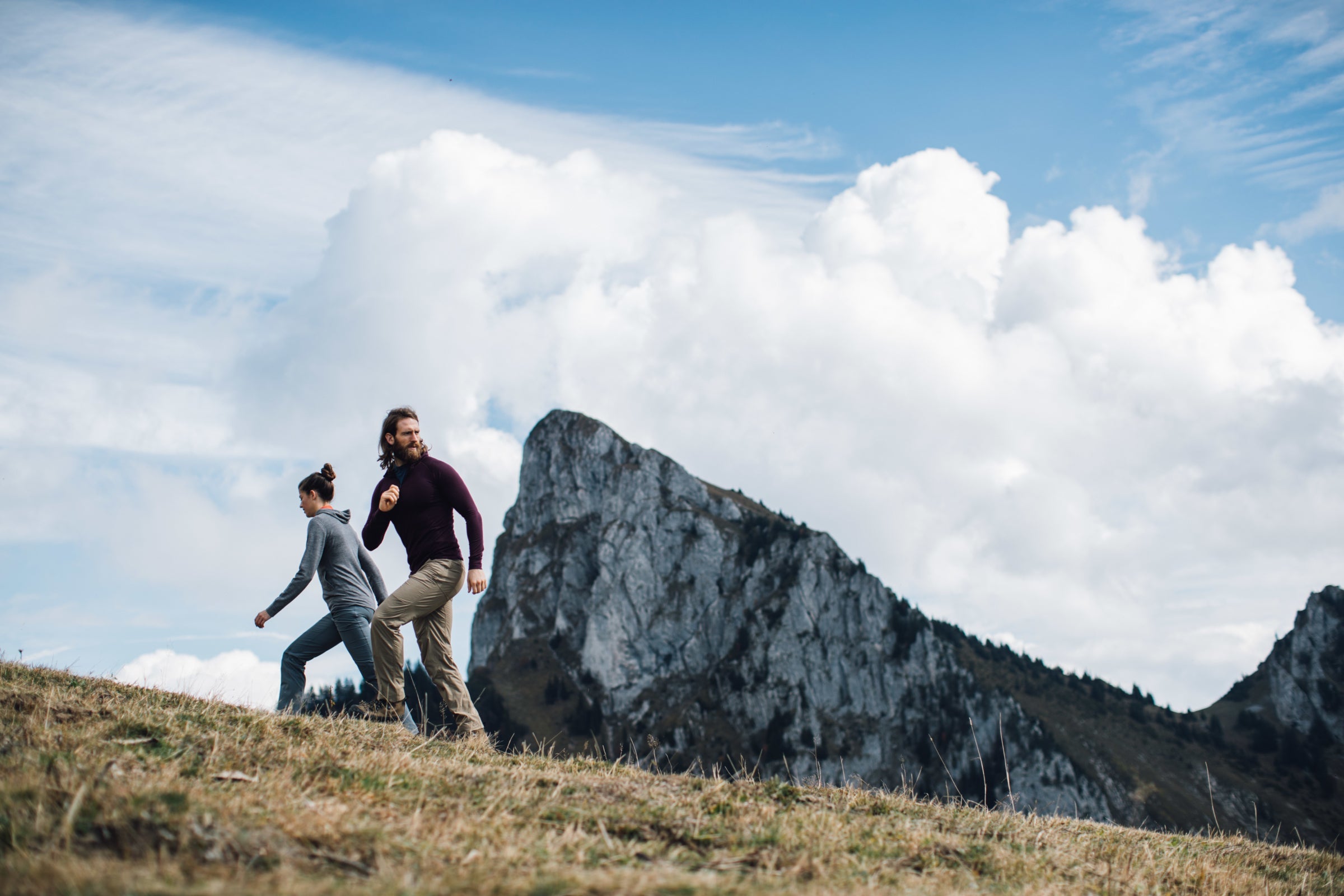 Two people hiking on a grassy hill with a mountain in the background