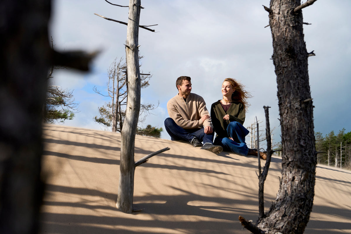 Two people sitting on a sandy dune outdoors