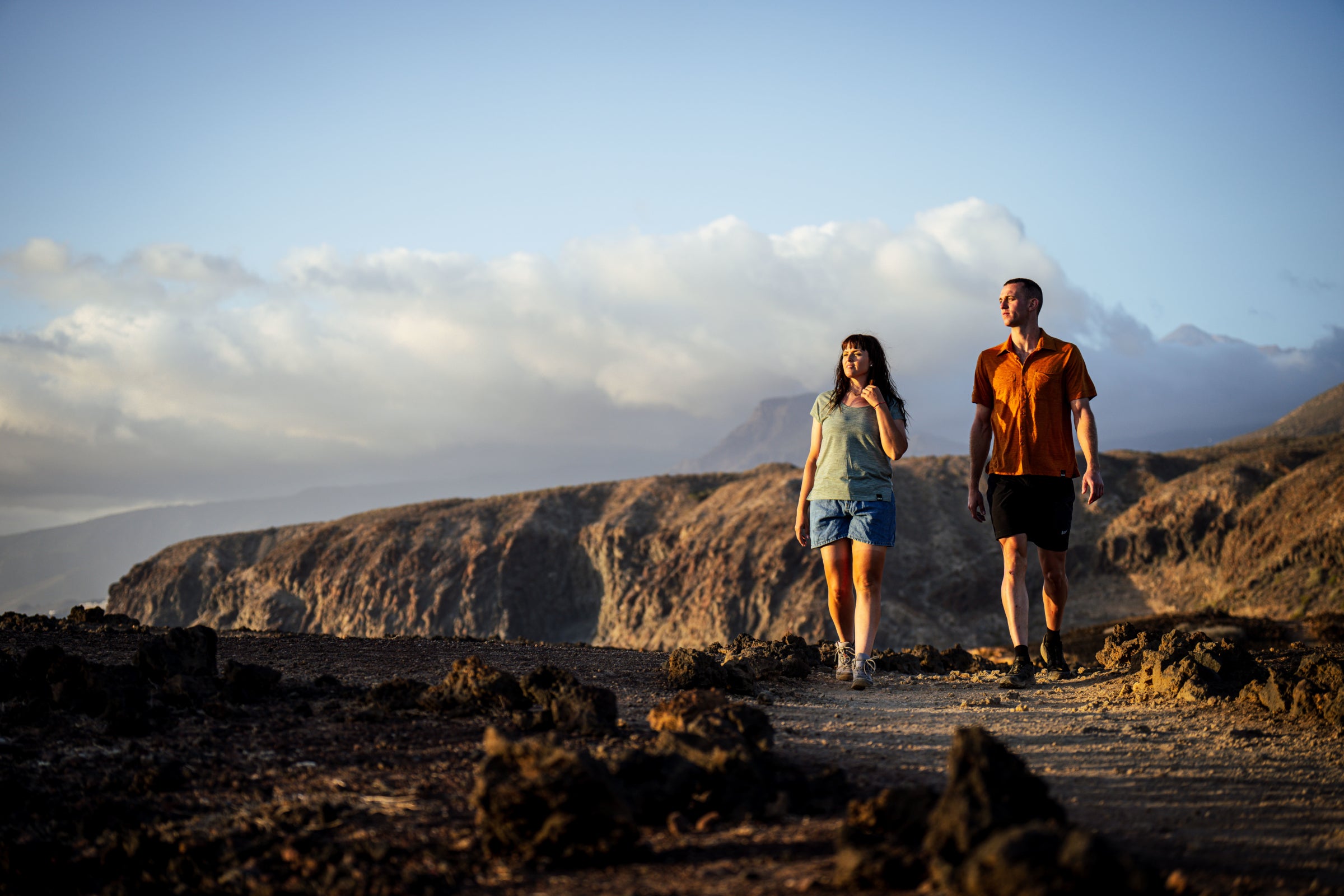 Man and woman hiking at golden hour in lightweight Merino clothing, with rocky cliffs in the background