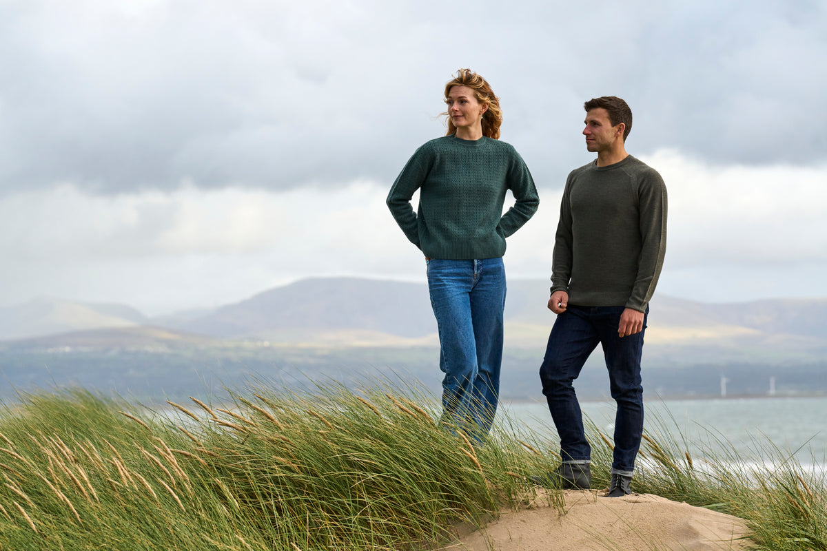 A man and a woman standing on a grassy dune overlooking a coastal landscape