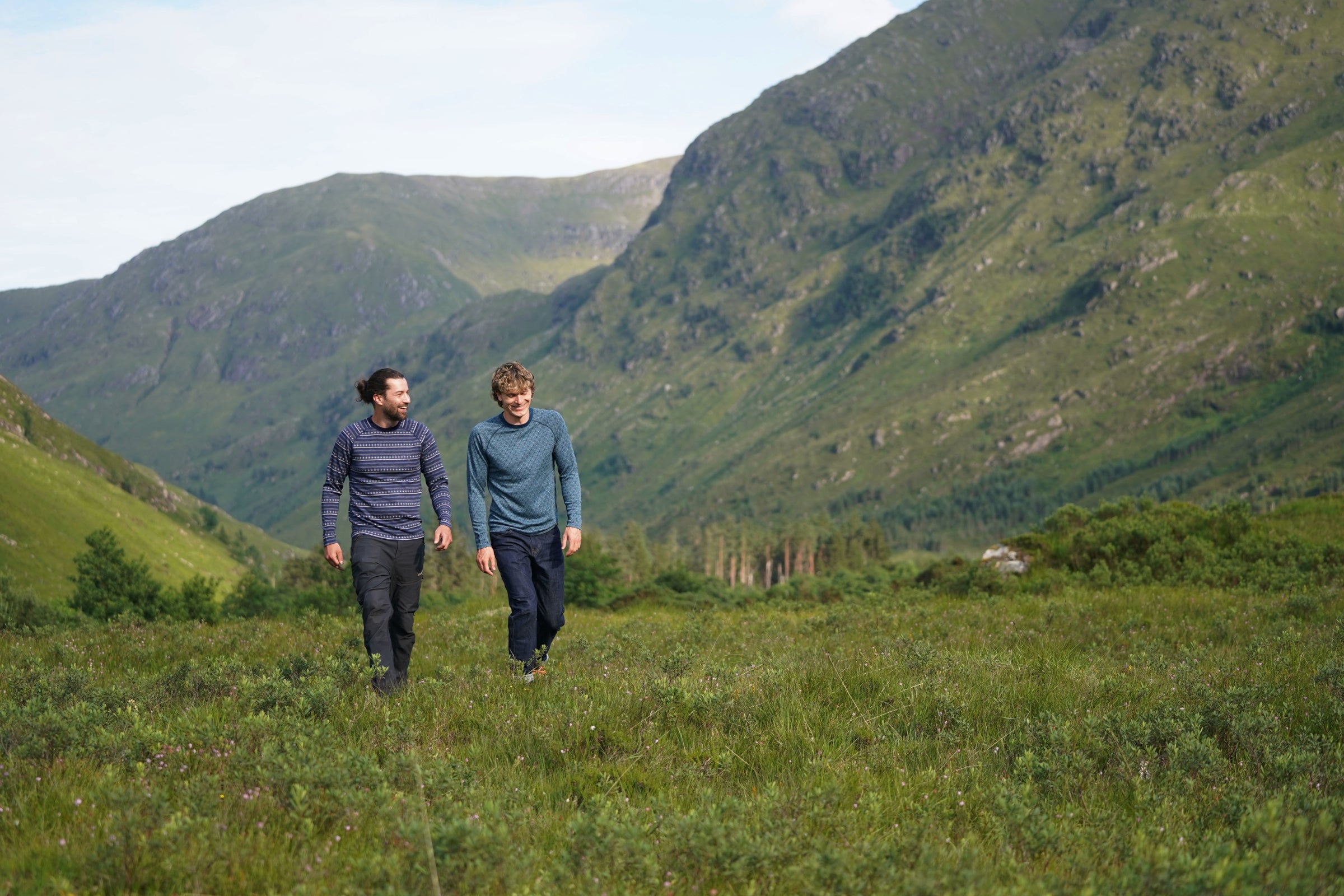 Two men hiking through a green mountain valley wearing Isobaa merino tops