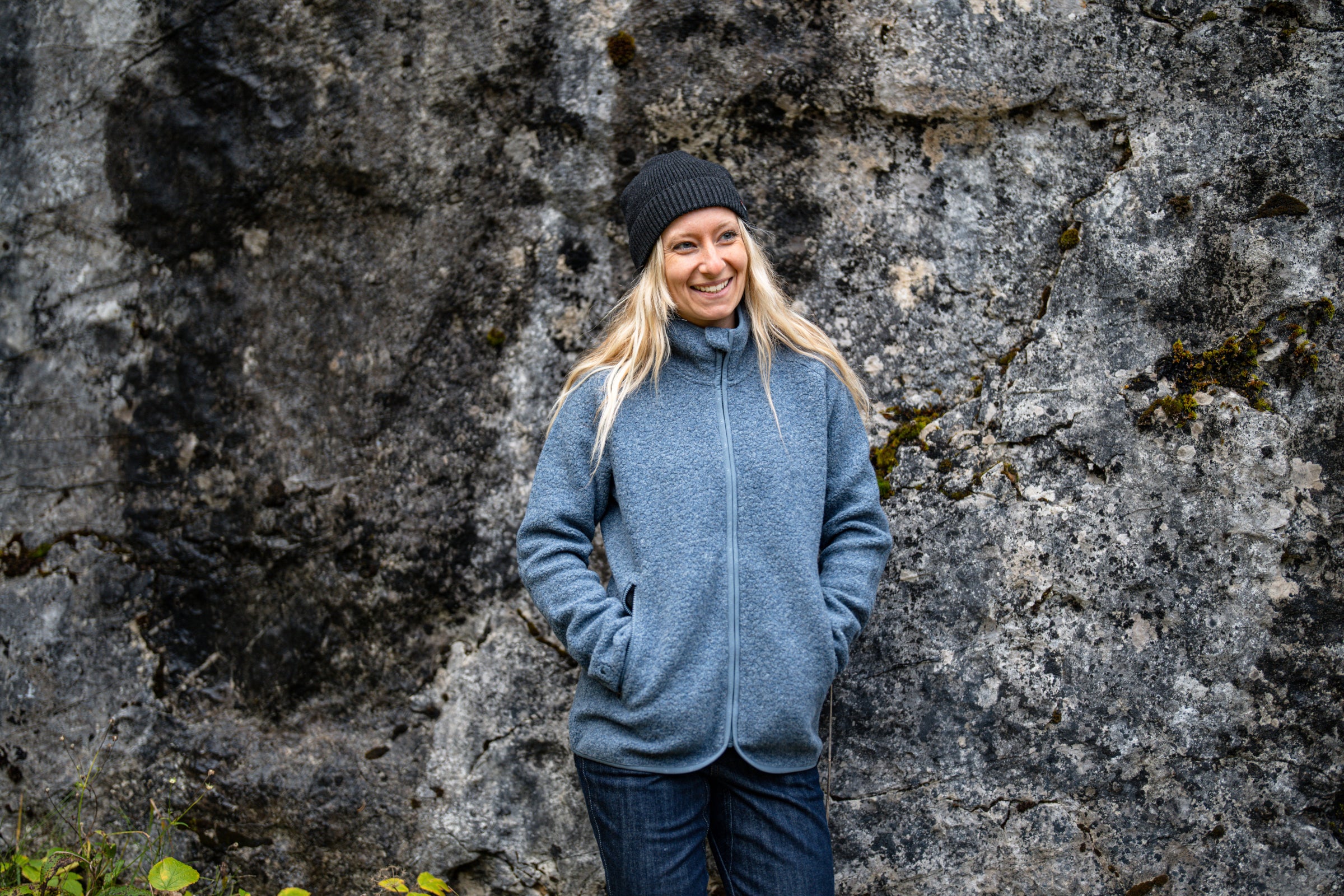 Woman standing against a rock wall wearing a grey fleece jacket