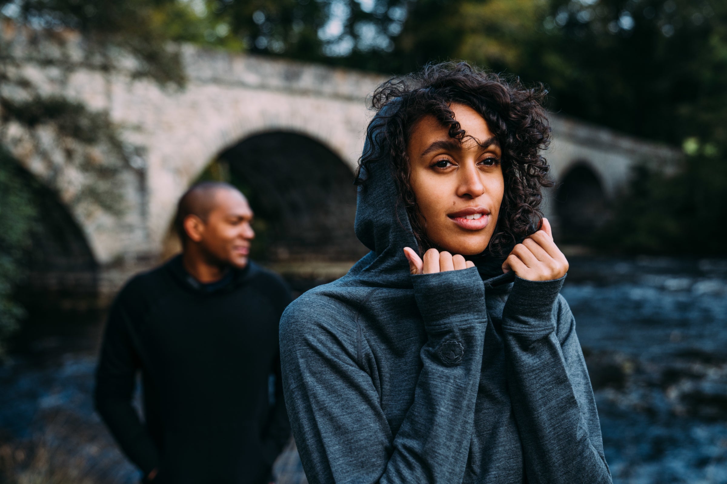 A woman wearing Merino wool hoodie near river, smiling and relaxed
