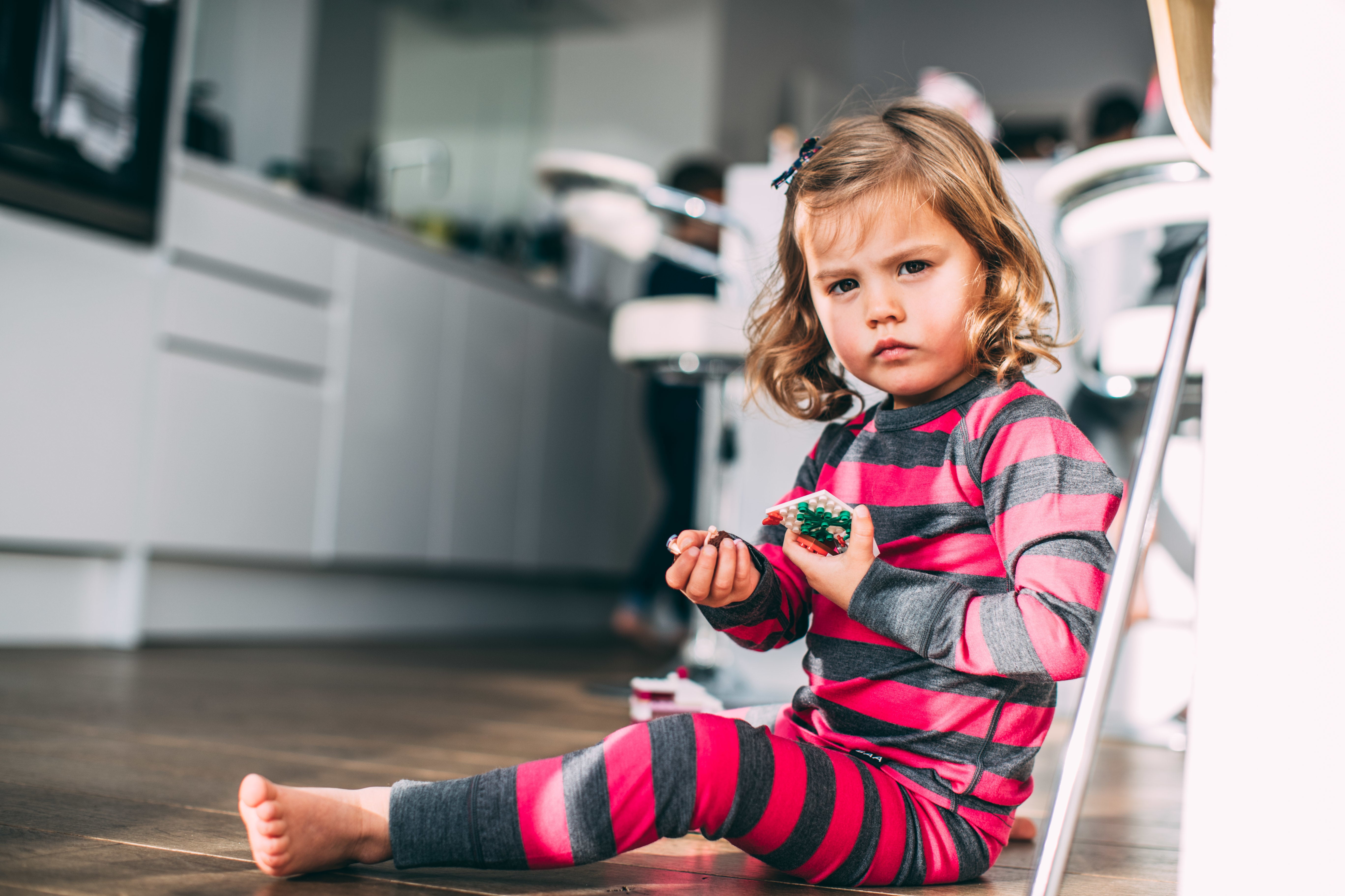 A child sitting indoors wearing striped Merino wool base layer