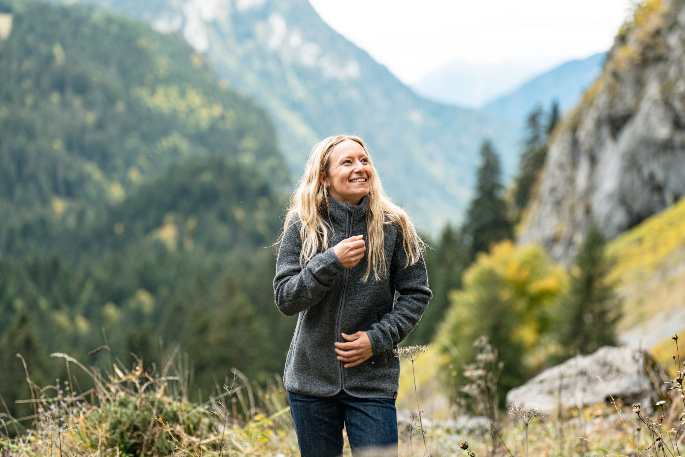 A woman smiling in Merino fleece jacket with forested mountain background