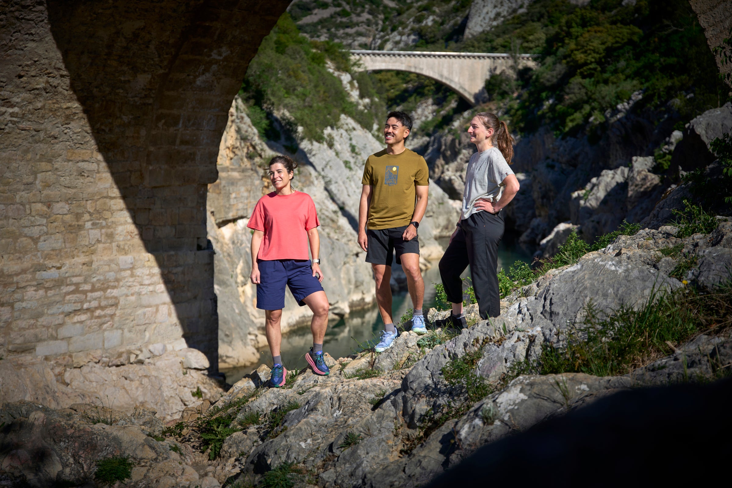 Three people standing on a rocky path with a stone arch and bridge in the background