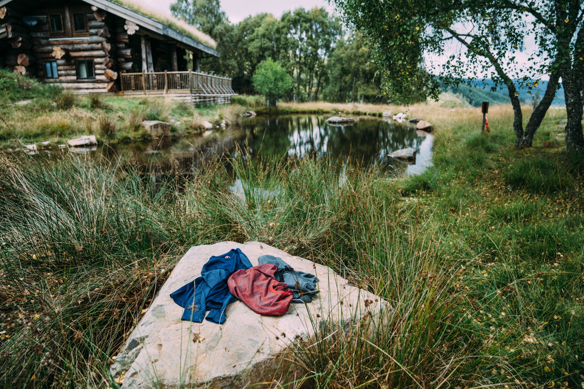 merino garments on a rock next to a pond near a log cabin